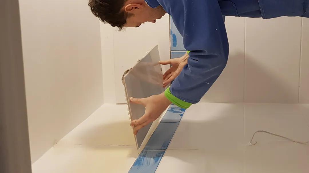 Romain adding a tile to a bathroom wall